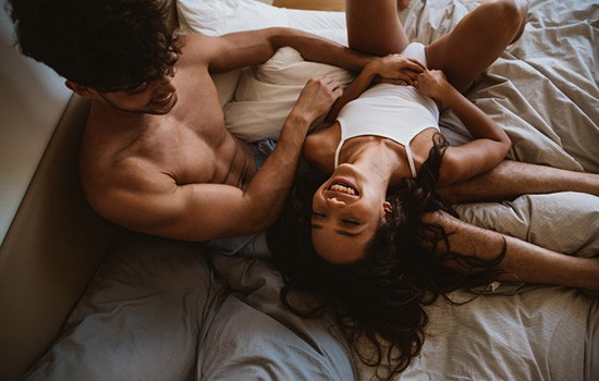 A woman and a man are smiling in bed while talking about double penetration.